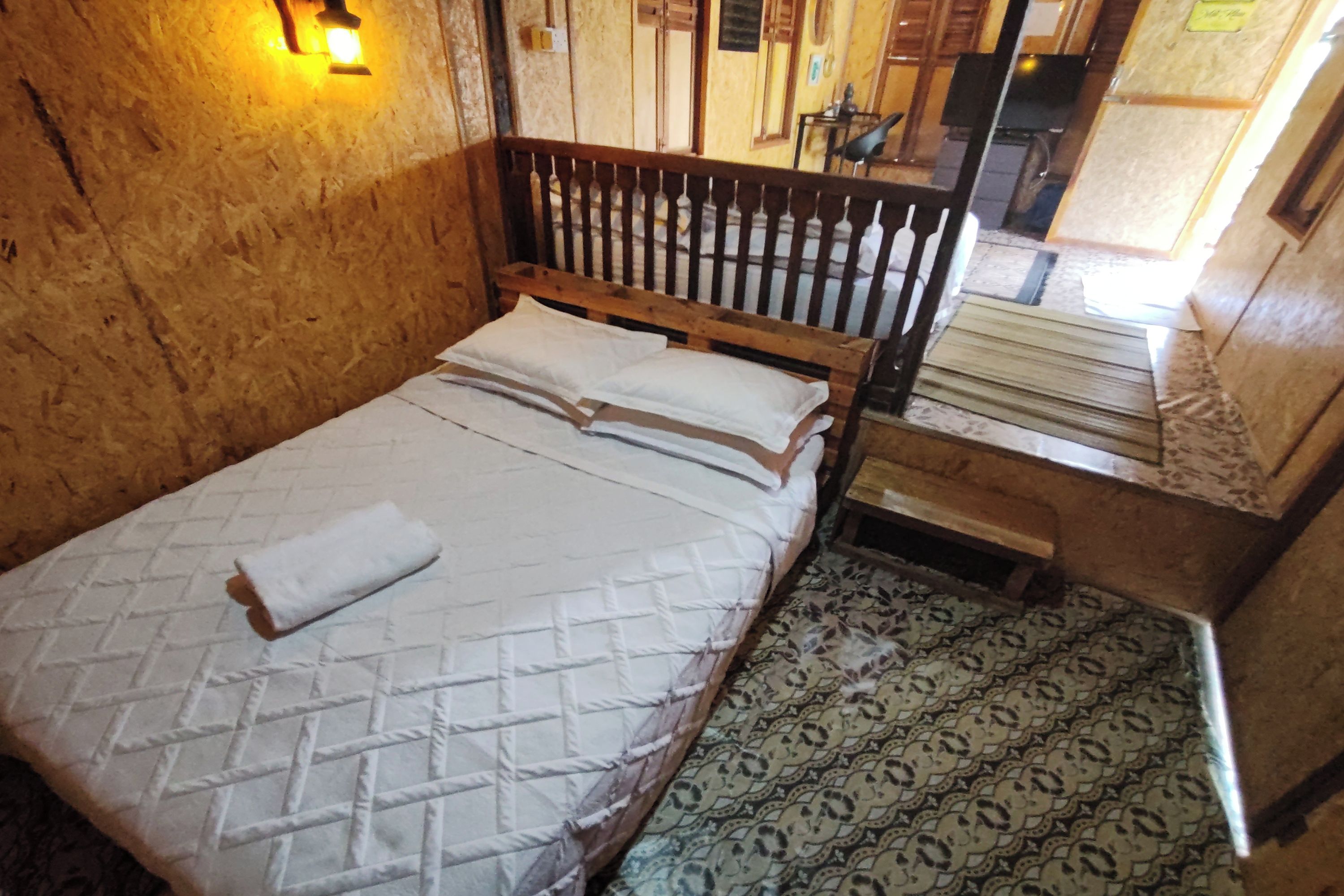 A wooden-framed bed with a quilted mattress and pillows, a small wooden nightstand, and patterned floor tiles.