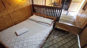 A wooden-framed bed with a quilted mattress and pillows, a small wooden nightstand, and patterned floor tiles.