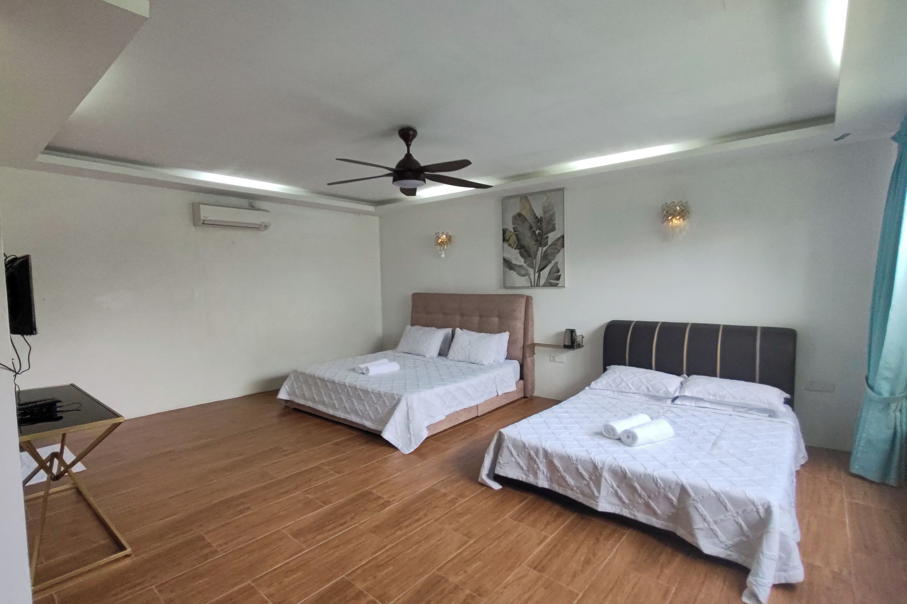 A room with two beds, a ceiling fan, a flat-screen TV, and a wooden floor.