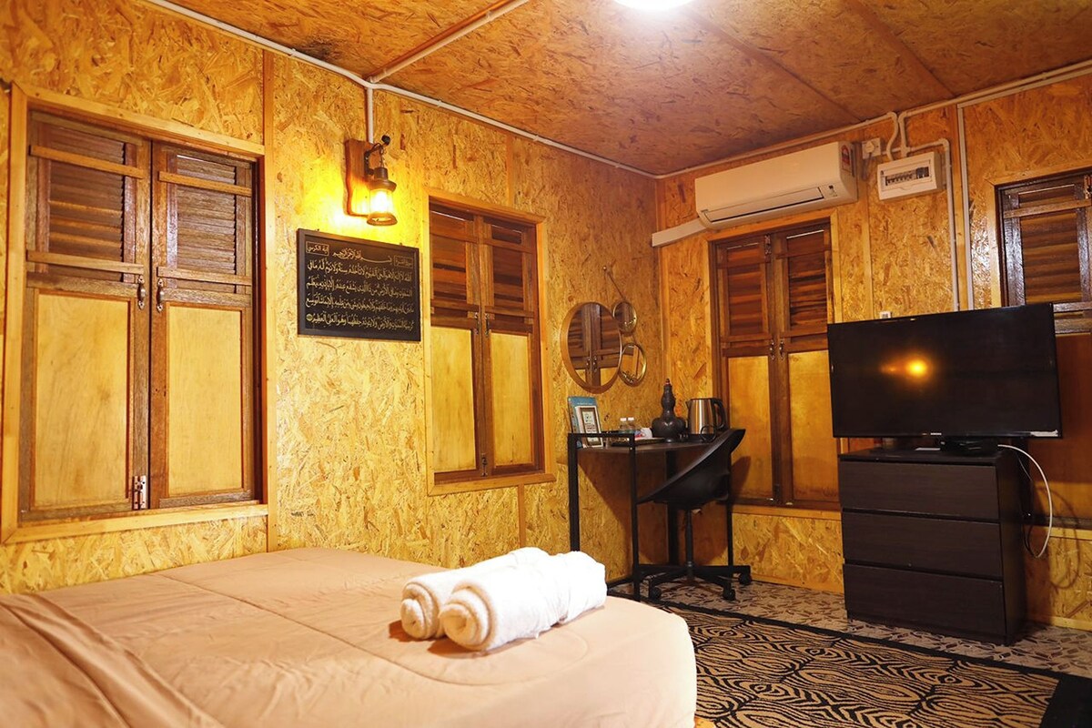 A room with a bed, a desk, a television, and wooden walls.