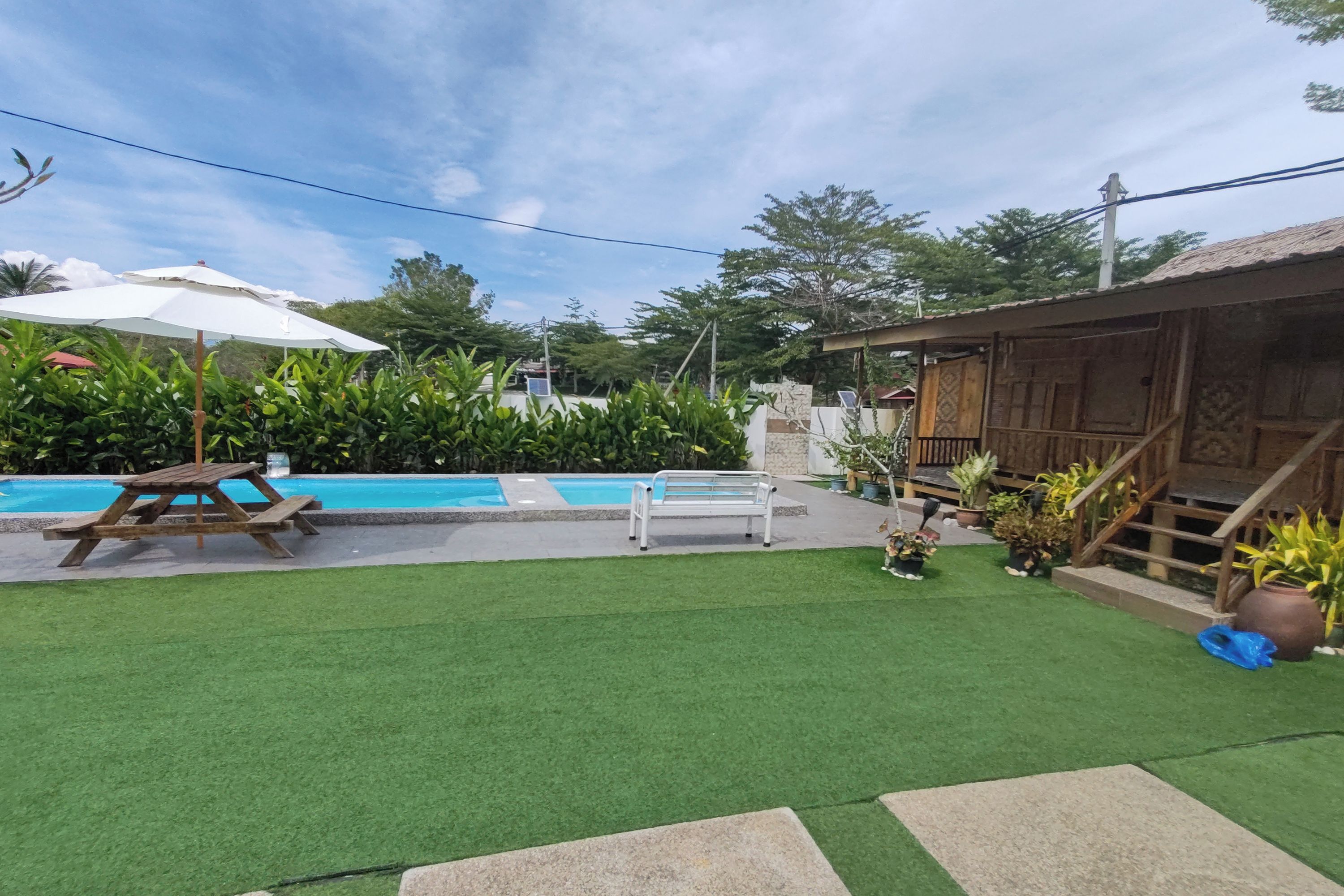 A backyard with a swimming pool, a wooden deck, and a house with a thatched roof.