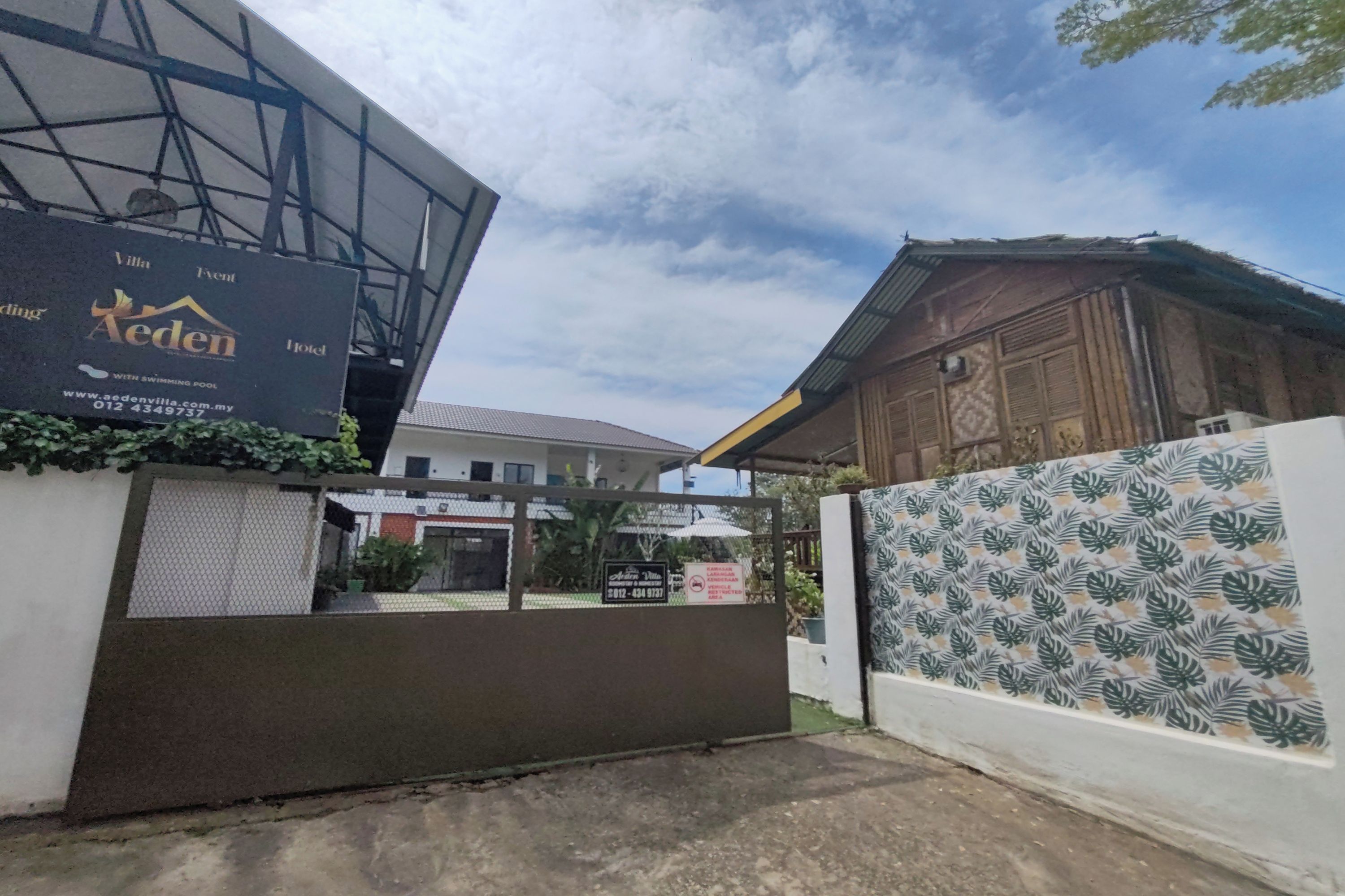A gated entrance to a hotel with a signboard, a wooden building, and a patterned wall.