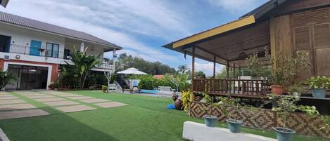A courtyard with artificial grass, a wooden deck, potted plants, and a building with a tiled roof.