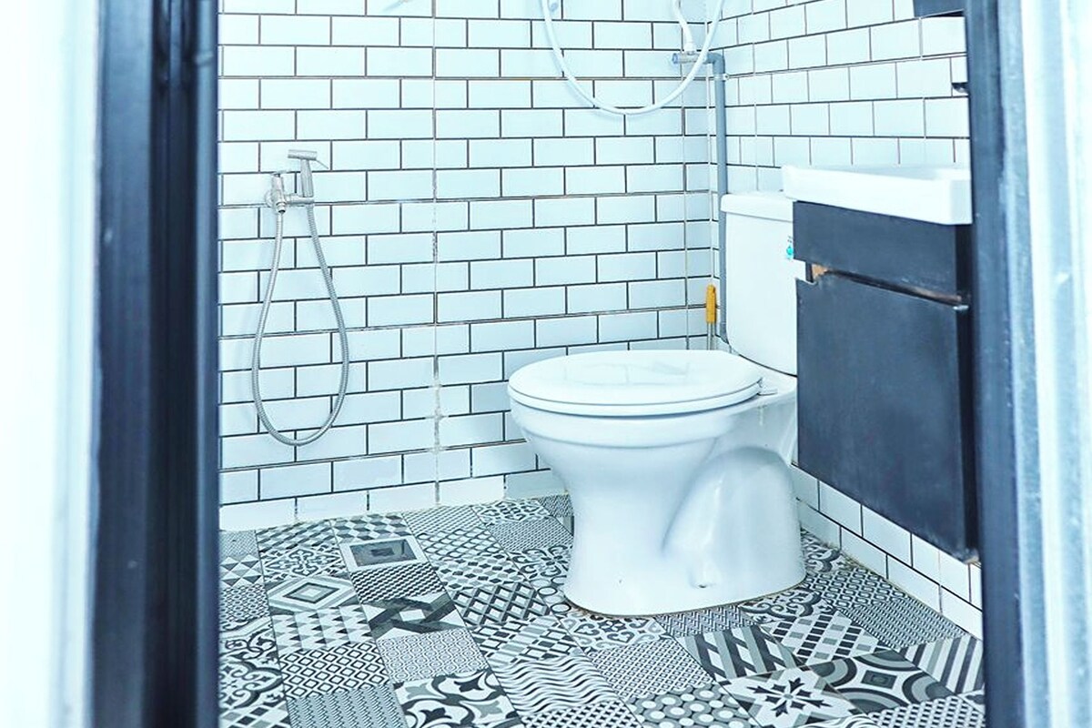 A bathroom with white tiled walls, a shower, a toilet, and patterned floor tiles.