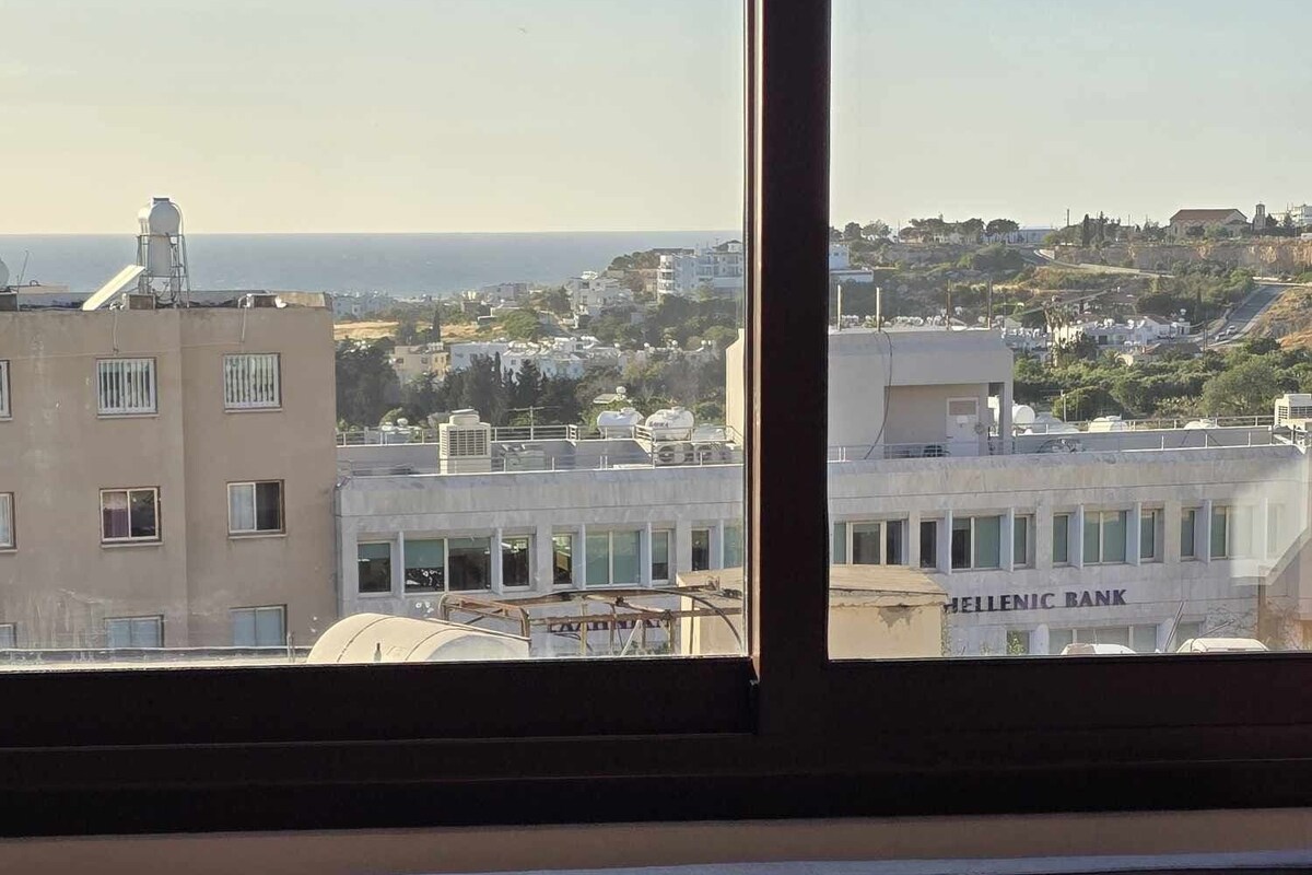 A room with a view of a cityscape, including a building labeled "HELLENIC BANK".