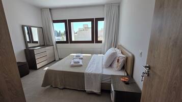 A modern bedroom with a large bed, a bedside table, a dresser, and a mirror.