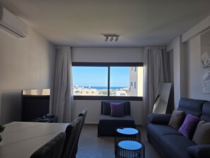 A modern living room with a large window, a dining area, and a sofa. - Kentrikon 1924 Boutique Hotel And Suites (Paphos)