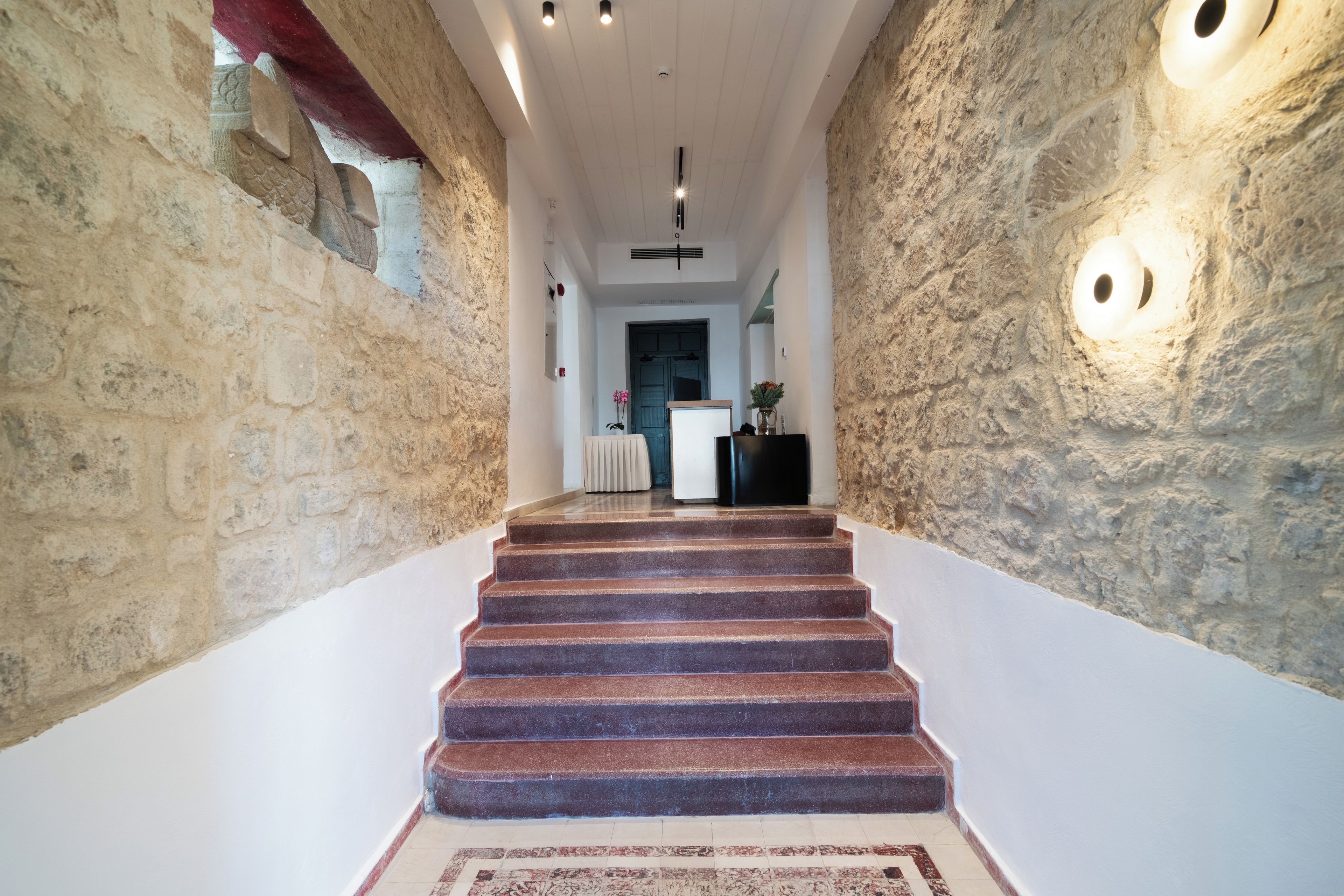 A staircase with stone walls and a carpeted floor leading to a room with a door and a radiator.