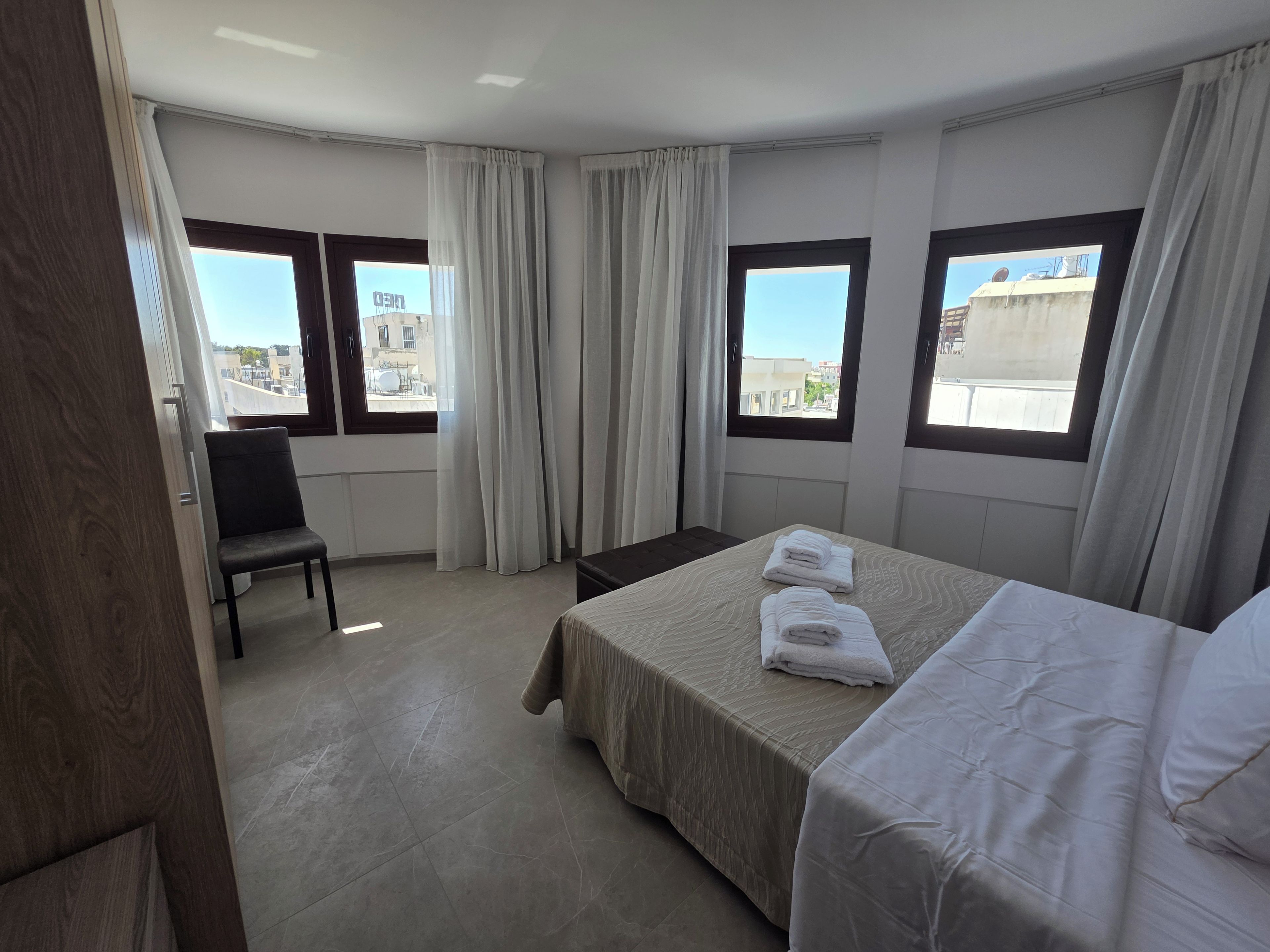 Una habitación de hotel con una cama, una silla y dos ventanas con cortinas.