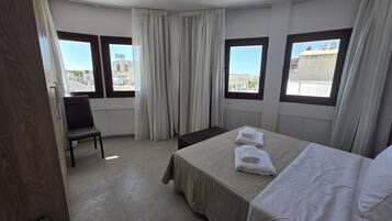 Una habitación de hotel con una cama, una silla y dos ventanas con cortinas.