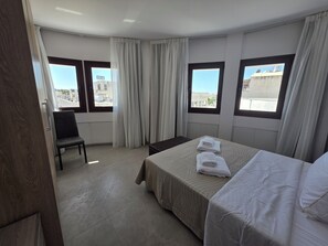 A hotel room with a bed, a chair, and two windows with curtains. - Kentrikon 1924 Boutique Hotel And Suites (Paphos)