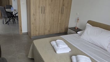 A hotel room with a bed, a wooden wardrobe, a desk with chairs, and a nightstand with a lamp.