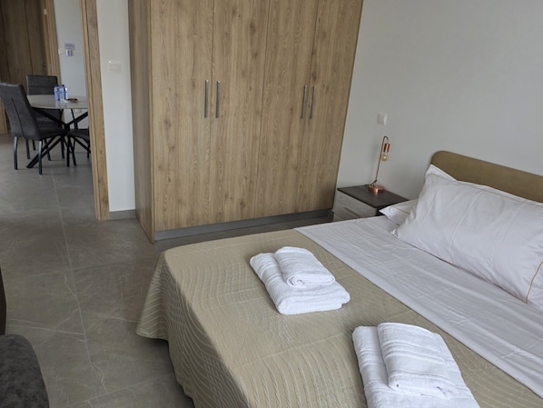 Una habitación de hotel con una cama, un armario de madera, un escritorio con sillas y una mesita de noche con lámpara.