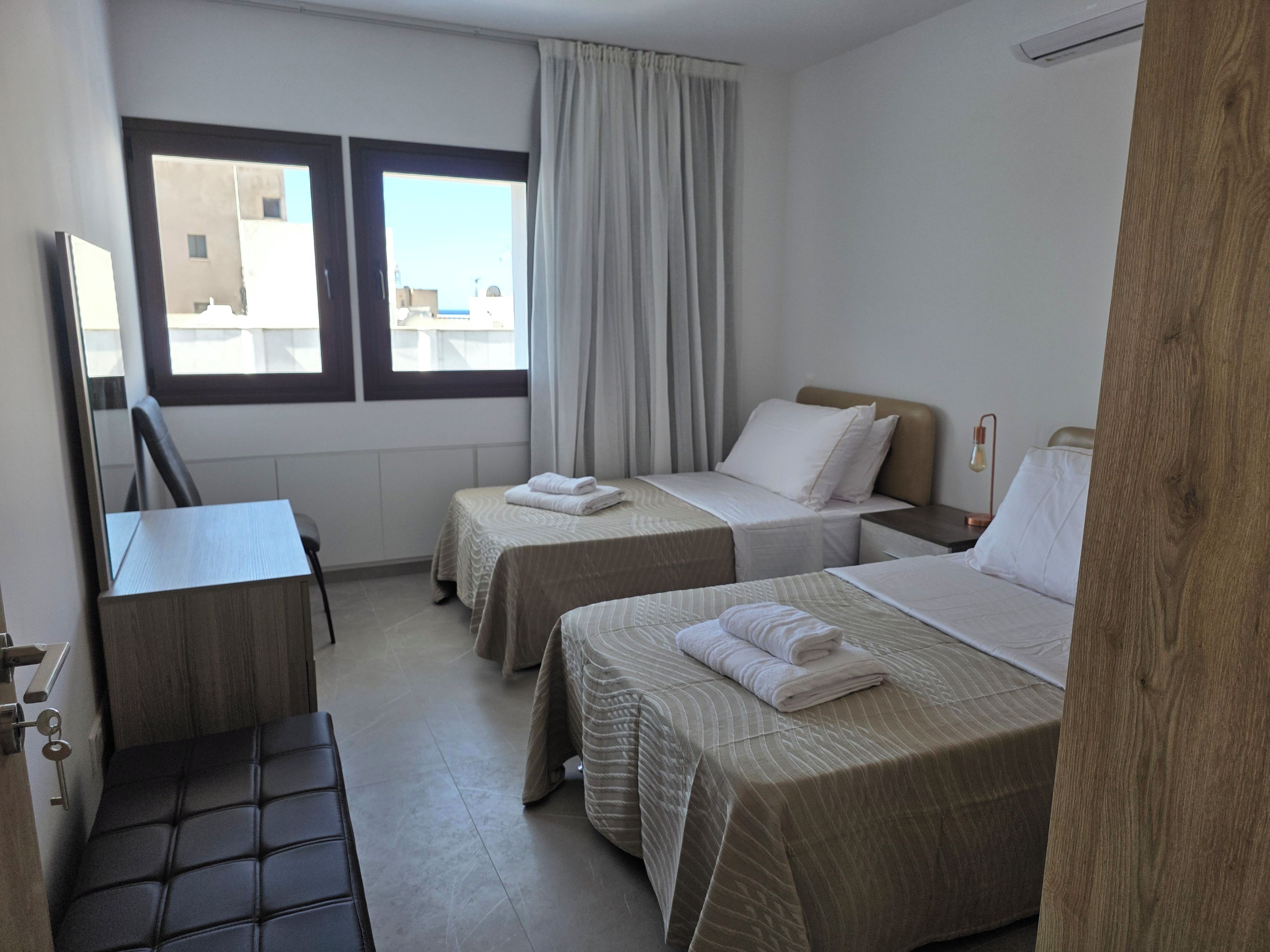 A hotel room with two beds, a desk, a chair, and a window with curtains.