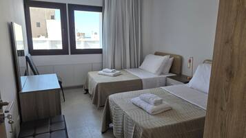 A hotel room with two beds, a desk, a chair, and a window with curtains.