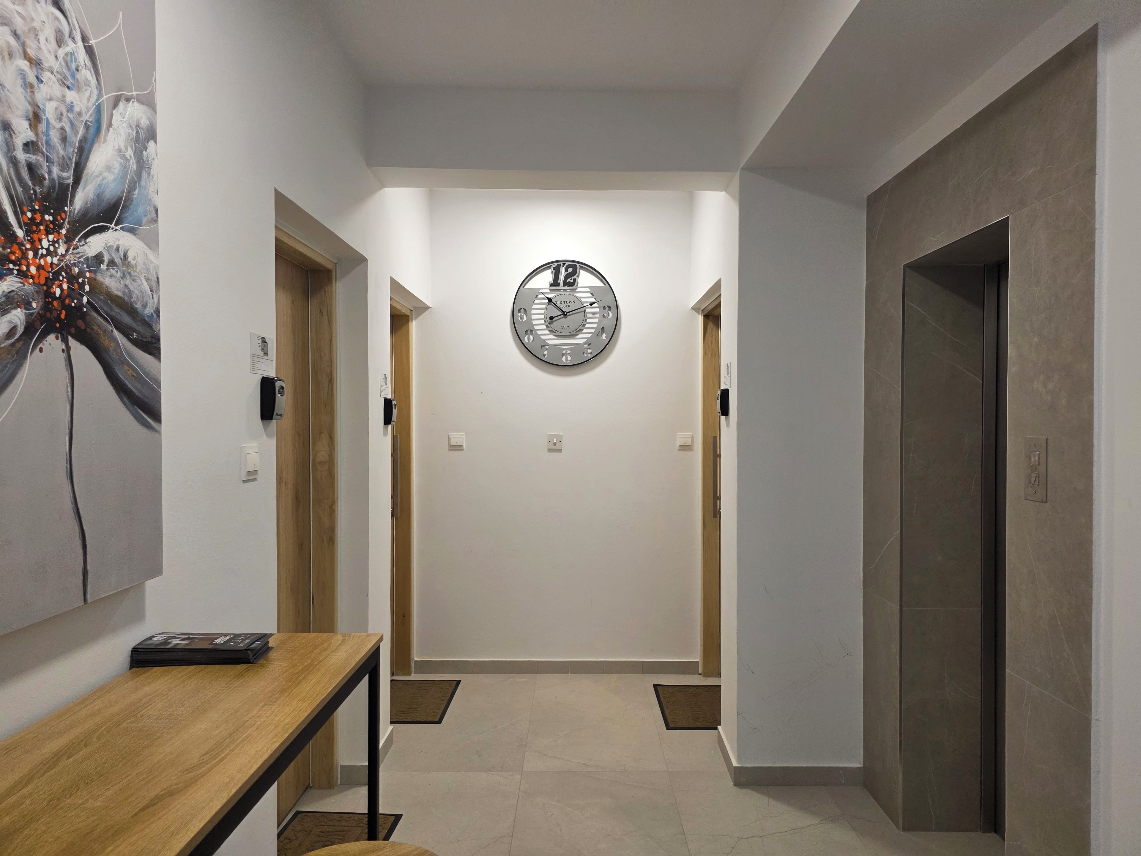 Un pasillo con un reloj, una mesa de madera y una puerta.