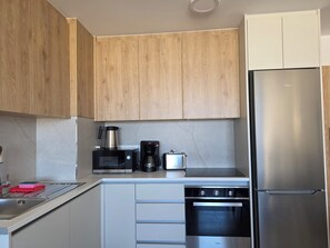 A modern kitchen with wooden cabinets, a Bosch microwave, a coffee maker, a stainless steel refrigerator, and a built-in oven. - Kentrikon 1924 Boutique Hotel And Suites (Paphos)