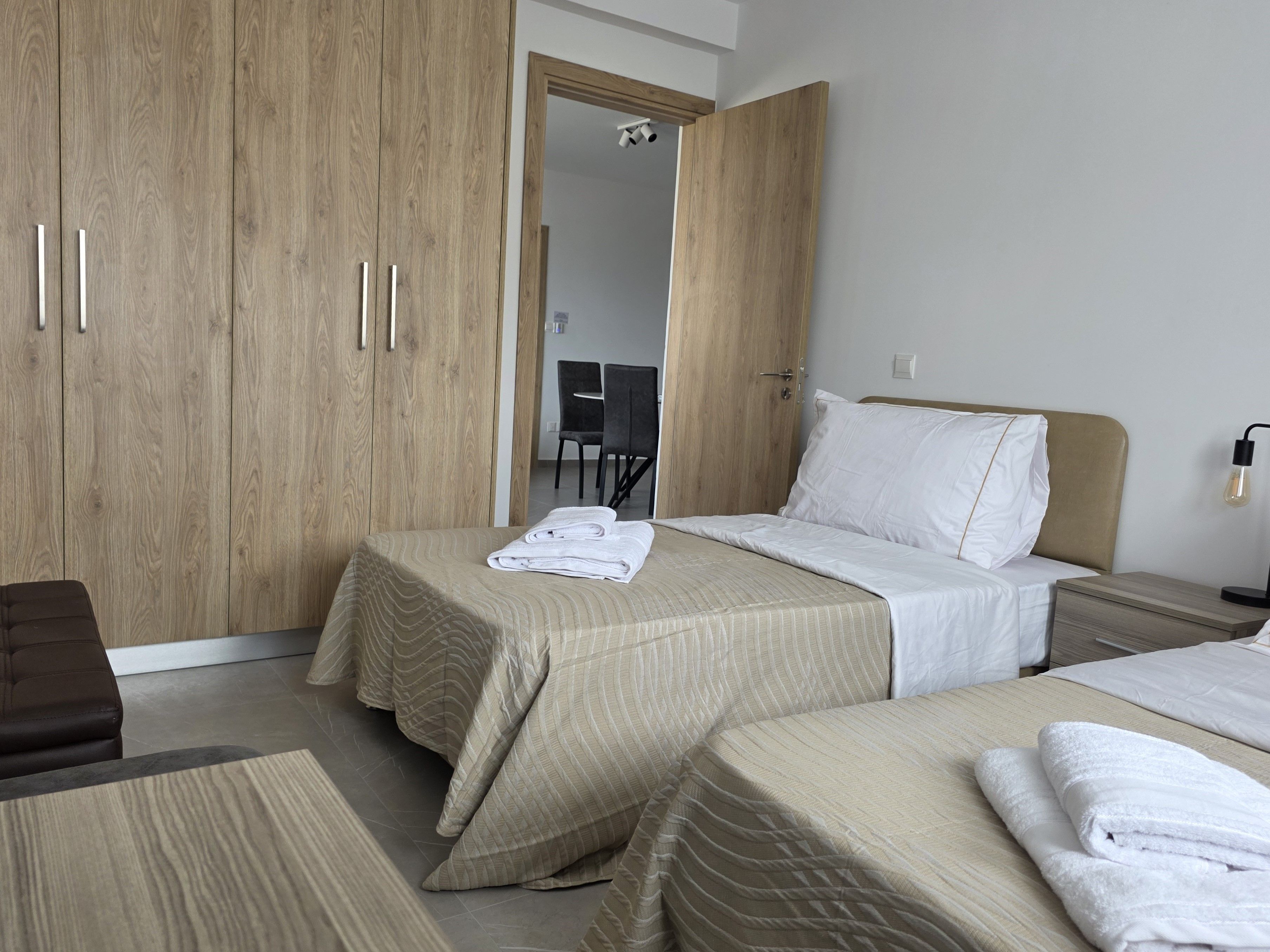 A hotel room with two beds, a wooden wardrobe, a desk, and a chair.