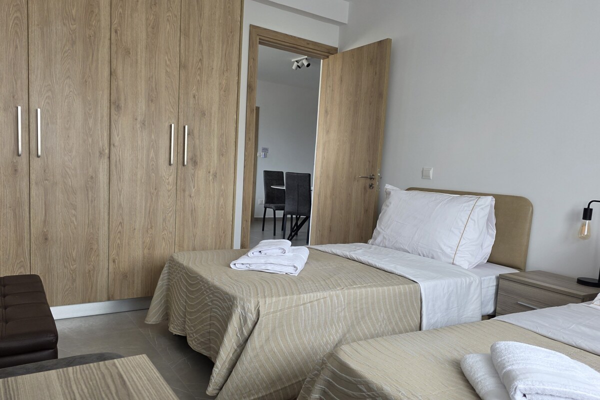 A hotel room with two beds, a wooden wardrobe, a desk, and a chair.