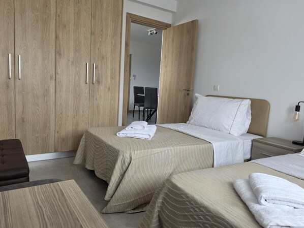 A hotel room with two beds, a wooden wardrobe, a desk, and a chair. - Kentrikon 1924 Boutique Hotel And Suites (Paphos)