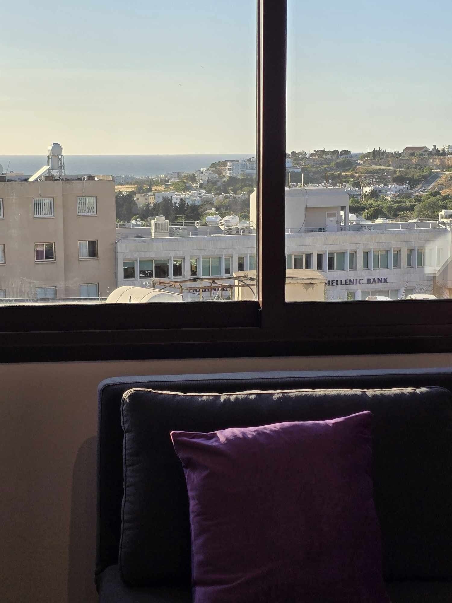 A room with a view of a cityscape, including a building labeled "HELLENIC BANK".