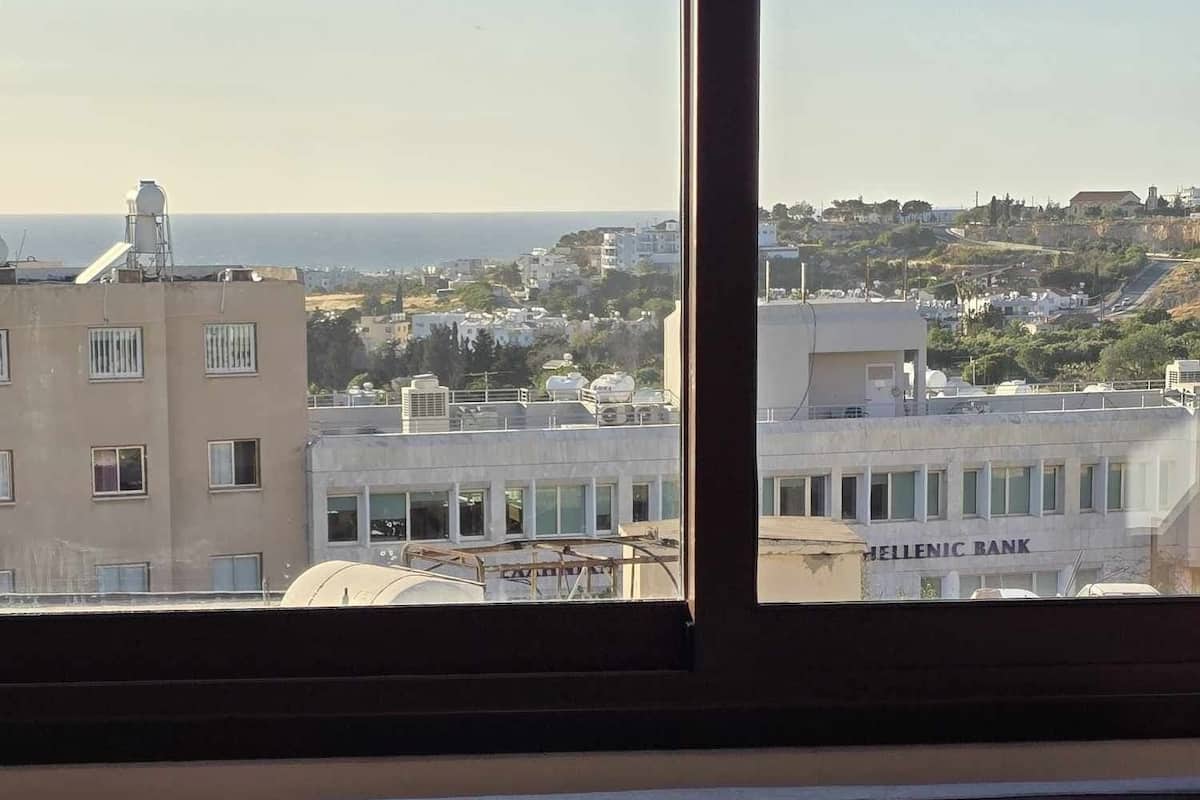 A room with a view of a cityscape, including a building labeled "HELLENIC BANK".