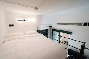 A modern hotel room with a bed, a wall-mounted light fixture, a window with a view, and a built-in air conditioning unit. - Kentrikon 1924 Boutique Hotel And Suites (Paphos)