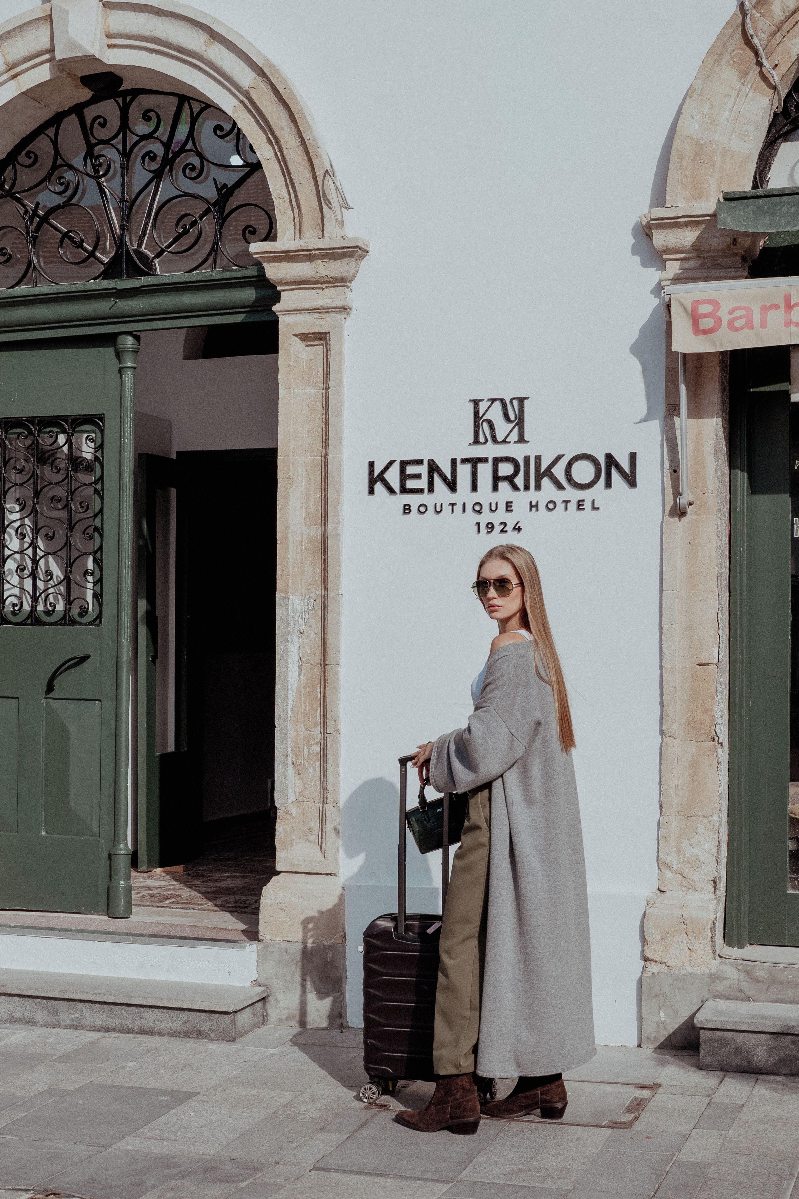 Una mujer está de pie frente a la entrada de un hotel boutique con un cartel que dice 'KENTRIKON BOUTIQUE HOTEL 1924'.