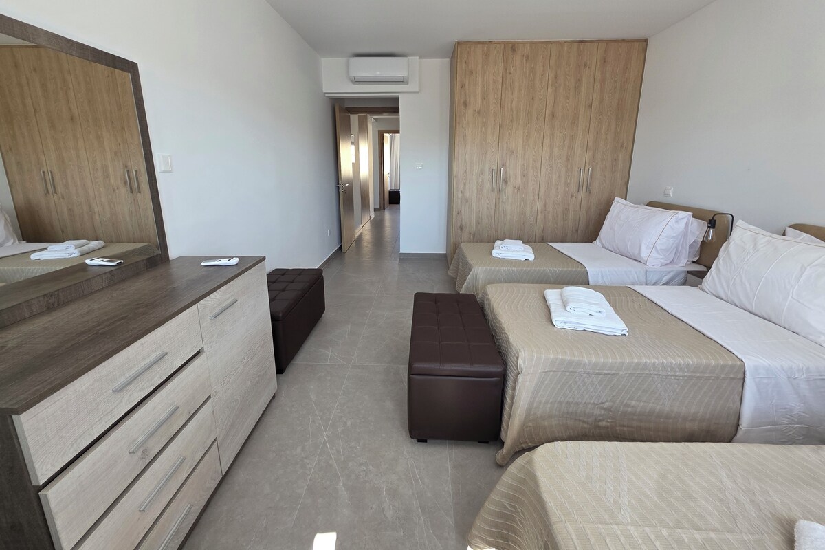A hotel room with two beds, a wooden wardrobe, a desk, and a bench.