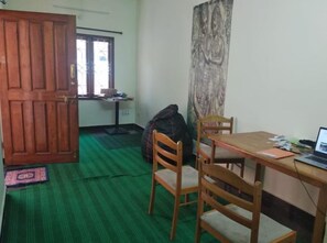 A room with a wooden door, a green carpet, a table with a laptop, and a chair. - Soloscape Stays Bengaluru (Bengaluru)