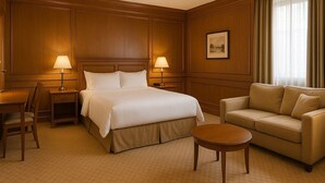 Una habitación de hotel con una cama, dos mesitas de noche con lámparas, un sofá, una silla y una pequeña mesa redonda.