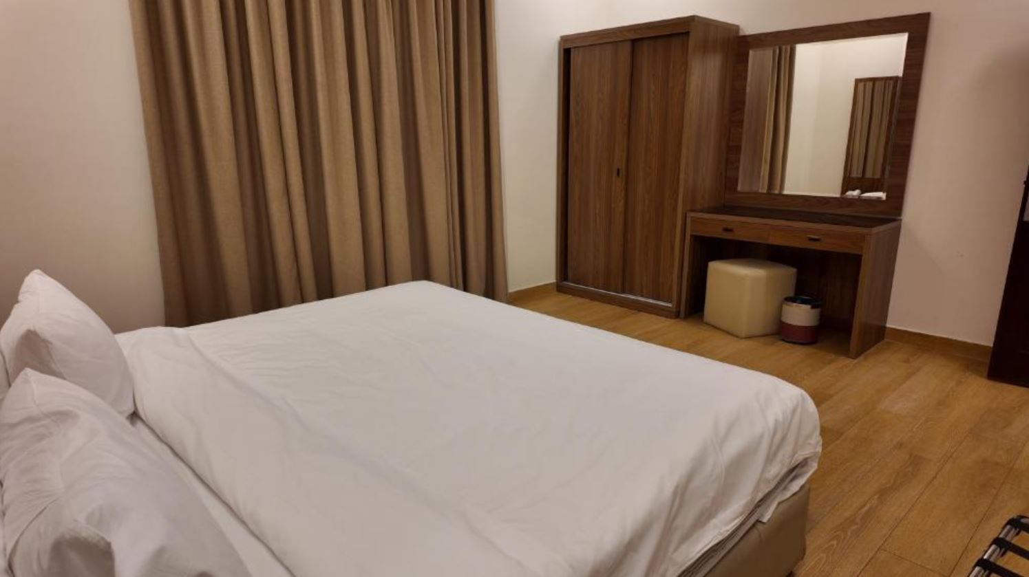 A hotel room with a bed, a wooden wardrobe, a mirror, and a small stool.