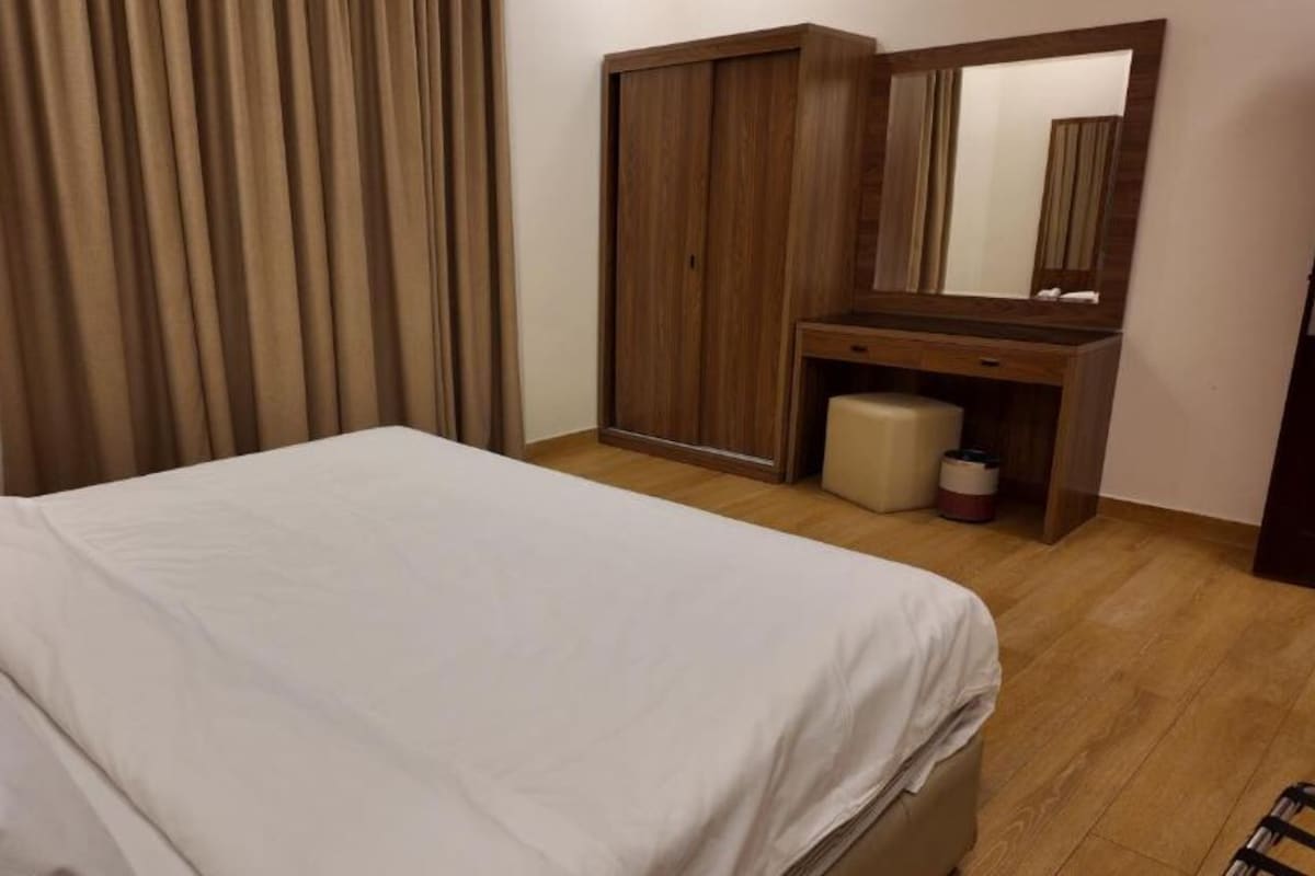 Ein Hotelzimmer mit einem Bett, einem Holzschrank, einem Spiegel und einem kleinen Hocker.
