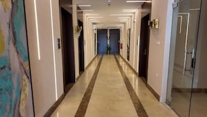 A long, well-lit hallway with a marble floor, doors on both sides, and a large abstract painting on the left. - Samt Inn Al Narjis (Riyadh)