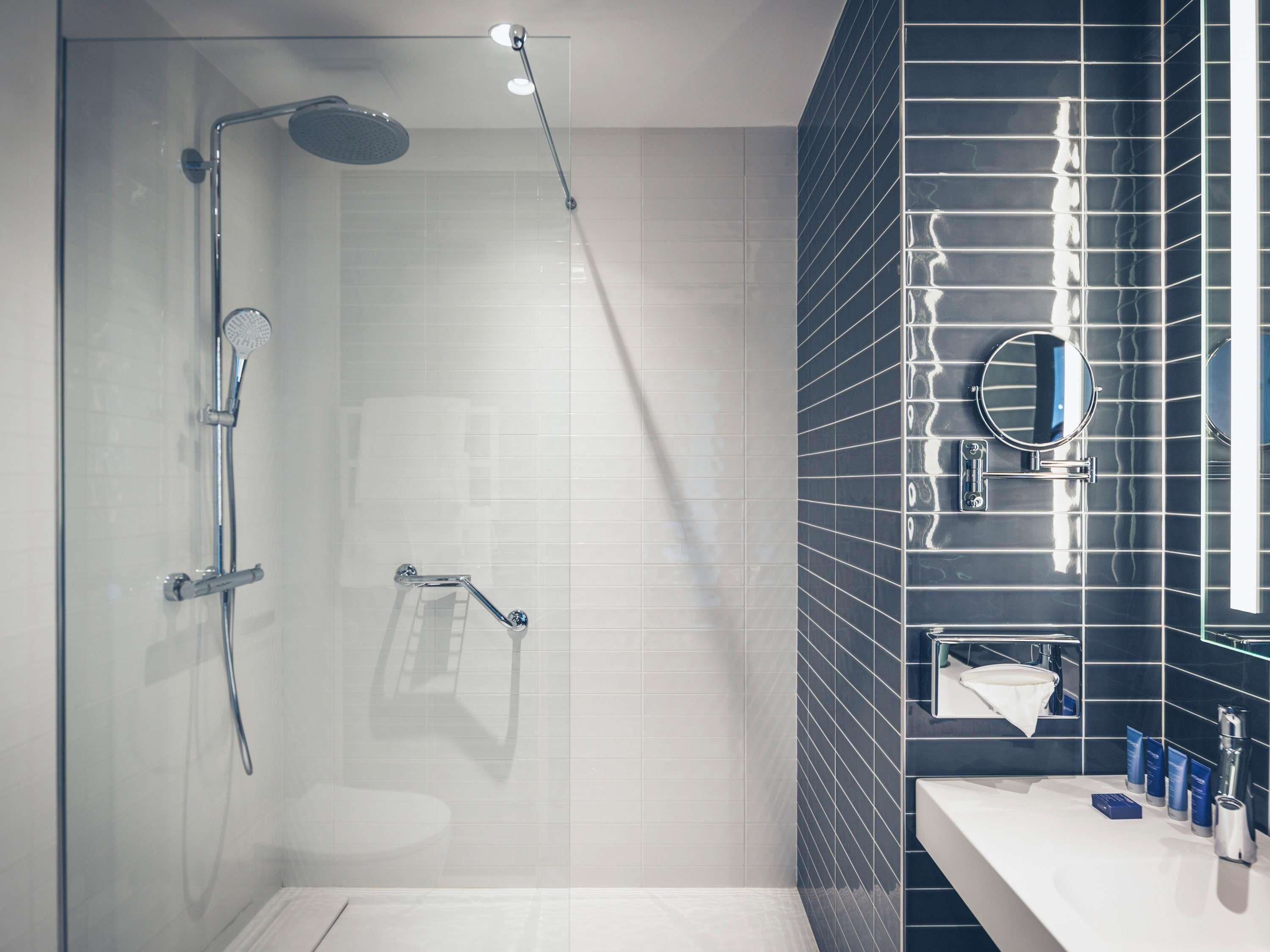 Un baño moderno con cabina de ducha de vidrio, un lavabo blanco y una pared revestida de baldosas oscuras.