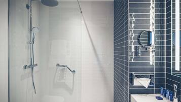 Un baño moderno con cabina de ducha de vidrio, un lavabo blanco y una pared revestida de baldosas oscuras.