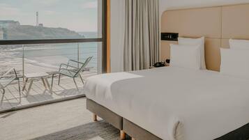 Une chambre d’hôtel avec un grand lit, une table de chevet, un téléphone et une vue sur la plage.