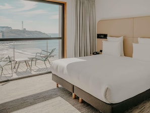 Une chambre d’hôtel avec un grand lit, une table de chevet, un téléphone et une vue sur la plage.