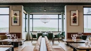 A restaurant with a long bench seating area, tables with chairs, and large windows offering a view of the outdoors. - Sainte-barbe Hotel Spa Le Conquet-mgallery Collect (Le Conquet)
