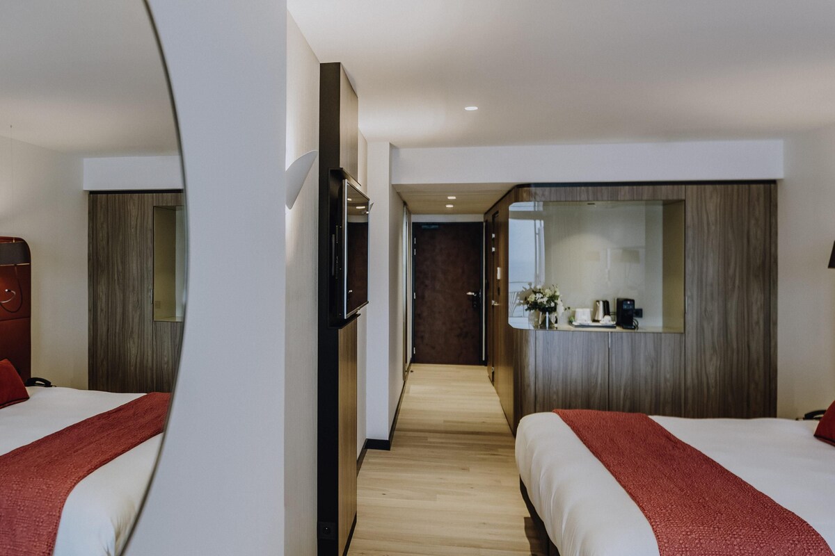 Habitación de hotel con dos camas, un televisor, un espejo y piso de madera.