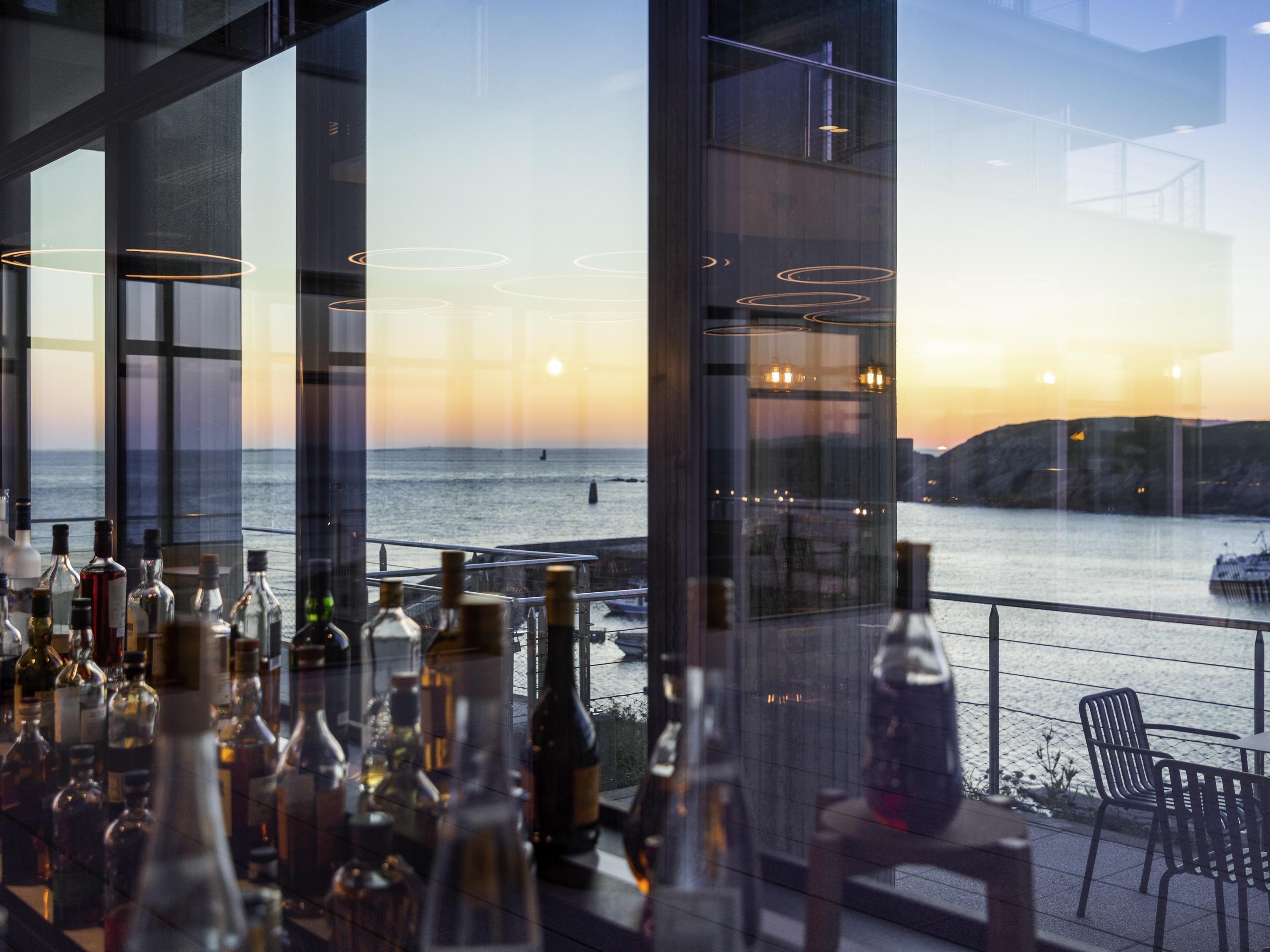 A bar area with bottles, a view of the sea, and a sunset.