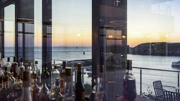 A bar area with bottles, a view of the sea, and a sunset.