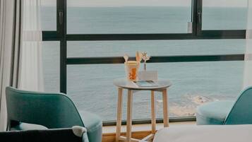 Une pièce dotée d’une grande fenêtre donnant sur la mer, de deux chaises, d’une petite table avec un menu, et offrant une vue sur la côte.