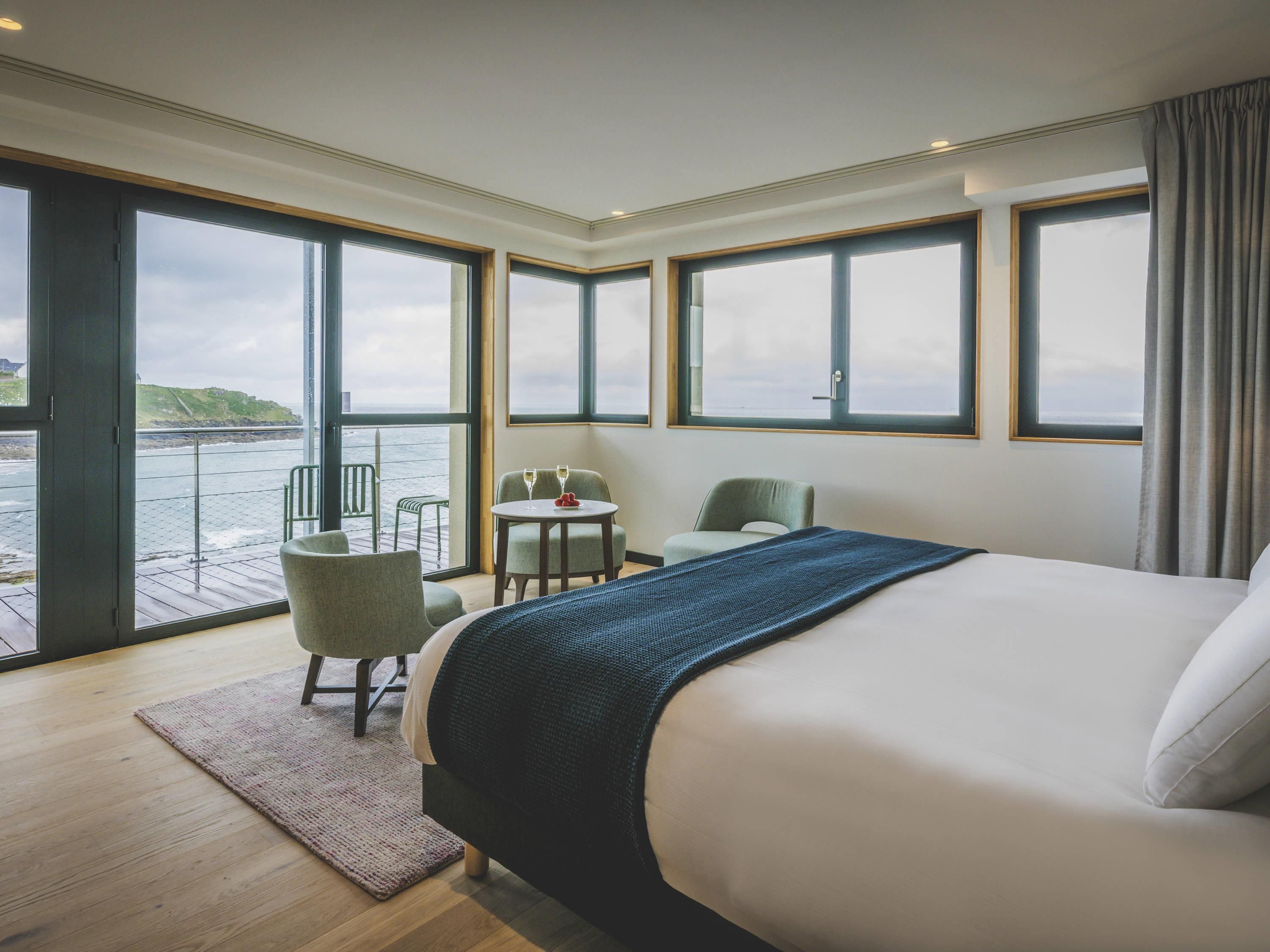 Une chambre d’hôtel avec un grand lit, une petite table avec deux chaises et une vue sur la mer.