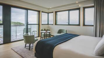 Une chambre d’hôtel avec un grand lit, une petite table avec deux chaises et une vue sur la mer.