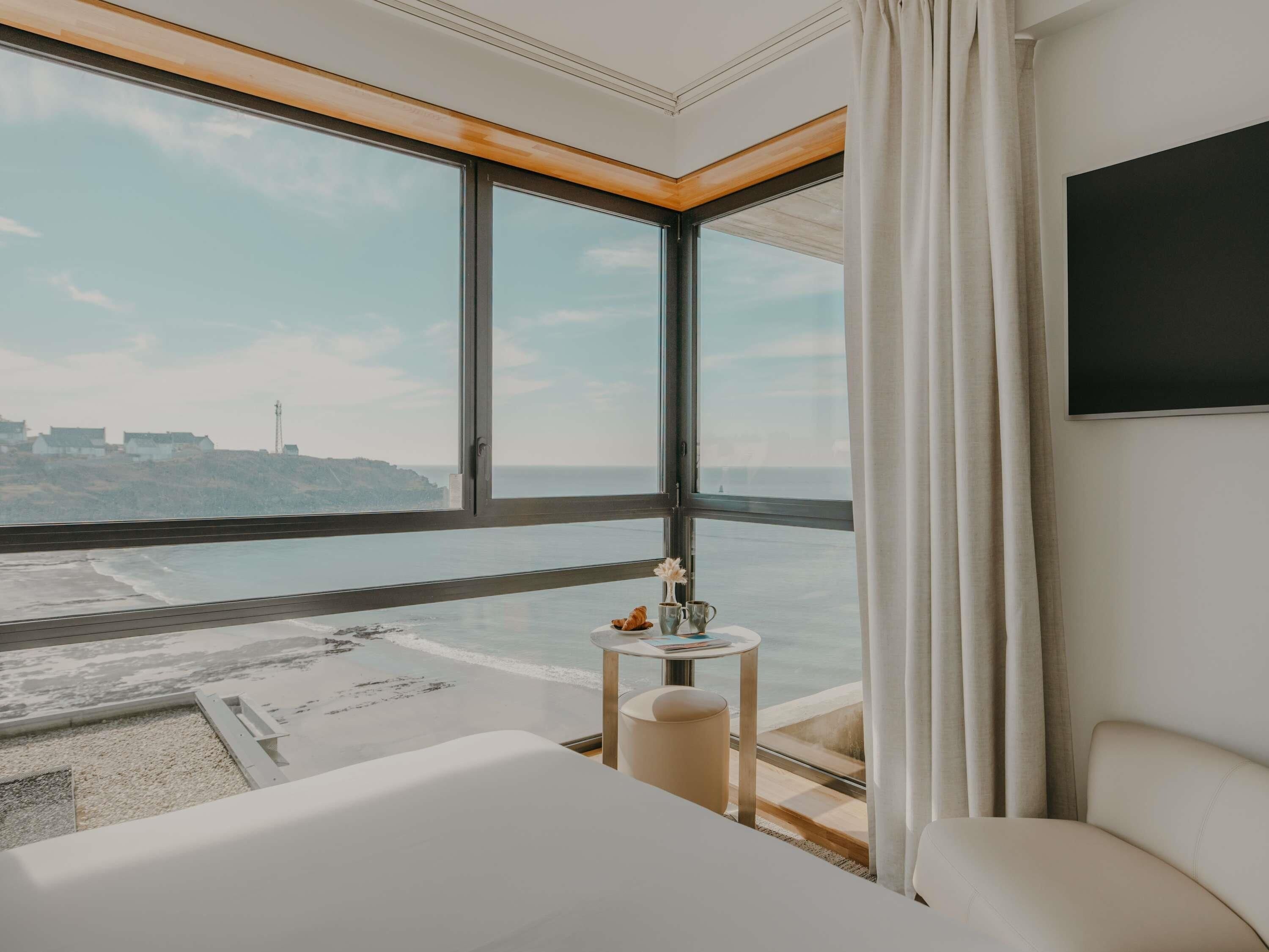 Een hotelkamer met een groot raam, een bed, een klein tafeltje met een vaas, en een televisie aan de muur.