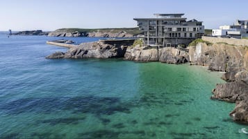 A coastal building with a modern architectural style, situated near a rocky shoreline with clear blue waters.