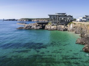 Un edificio costero de estilo arquitectónico moderno, ubicado cerca de una costa rocosa con aguas azules cristalinas.