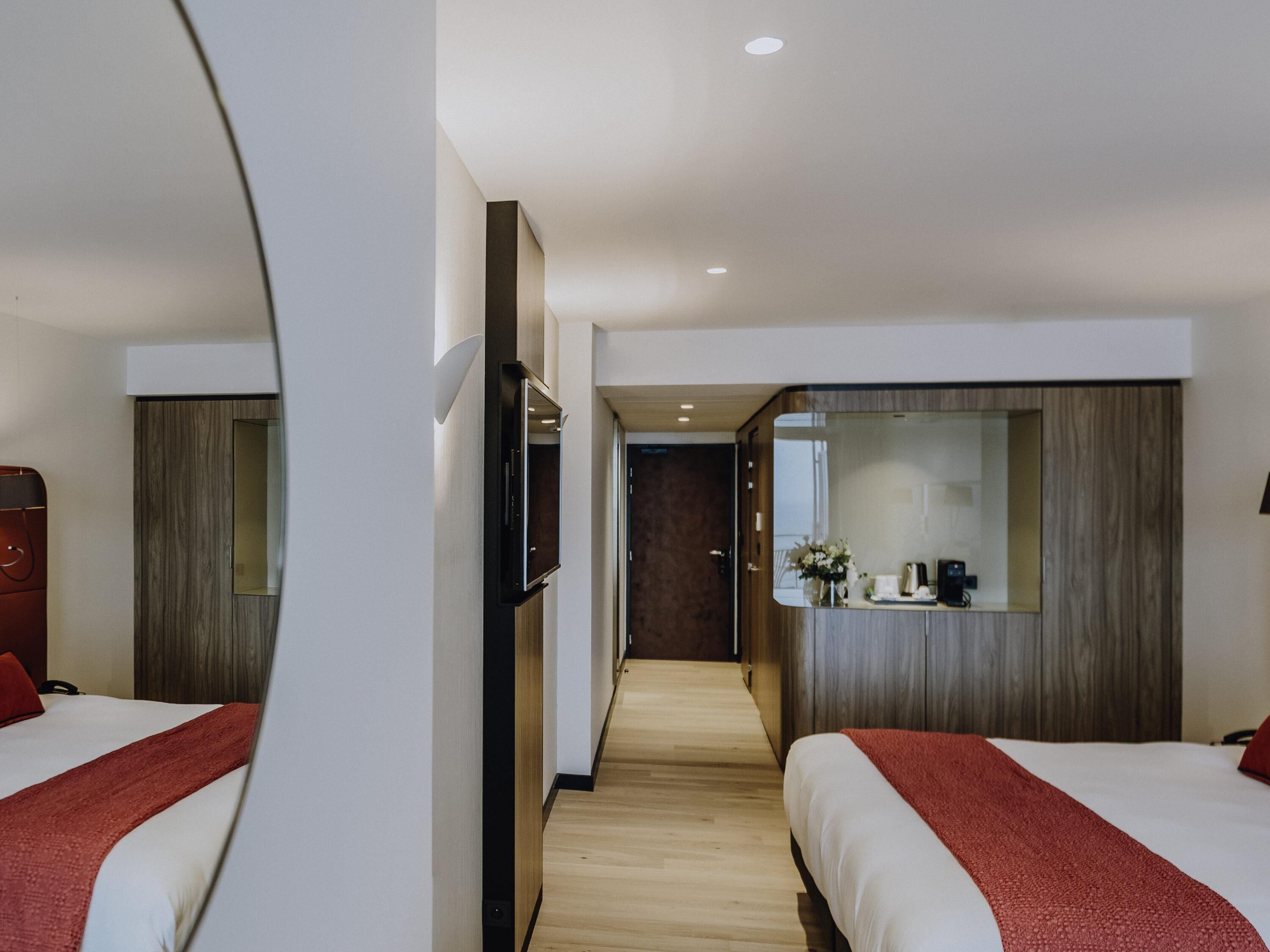 A hotel room with two beds, a TV, a mirror, and a wooden floor.