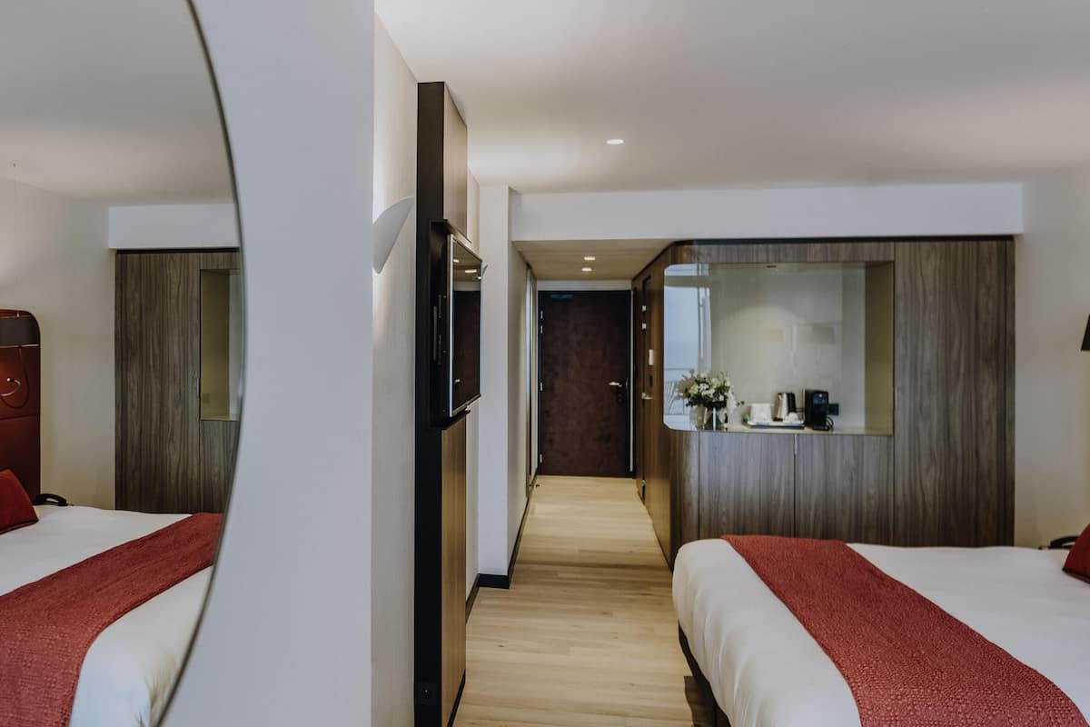 A hotel room with two beds, a TV, a mirror, and a wooden floor.